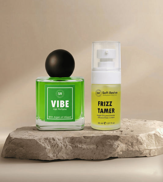 Two hair care products, 'Vibe' hair perfume and 'Frizz Tamer' serum, on a stone surface with a neutral background.