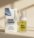 Soft Revive Frizz Tamer hair product shown with its white and blue retail box next to the clear bottle containing pale yellow oil, on a warm beige surface with soft shadows.